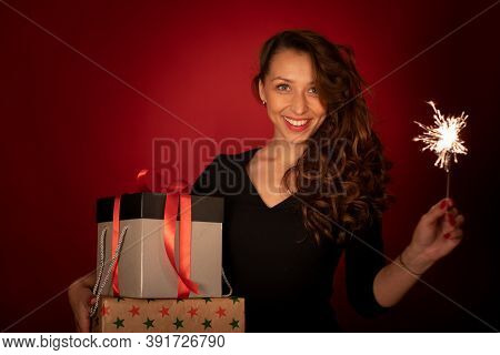 Smiling Pretty Woman With Holiday Gifts And Sparkler Posing On Red Background With Copy Space. Chris