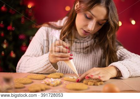 Christmas Bakery. Cute Brunette Girl Icing Christmas Gingerbread With Icing-sugar With Christmas Tre