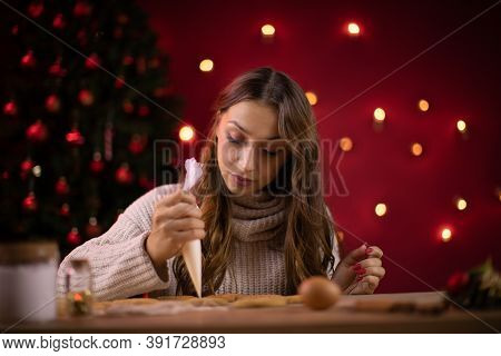 Portrait Of Pretty Long-haired Brunette Girl Decorating Christmas Cookies On Red Studio Background W
