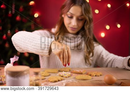 Portrait Of Pretty Brunette Girl Decorating Christmas Cookies With Christmas Tree And Red Xmas Decor