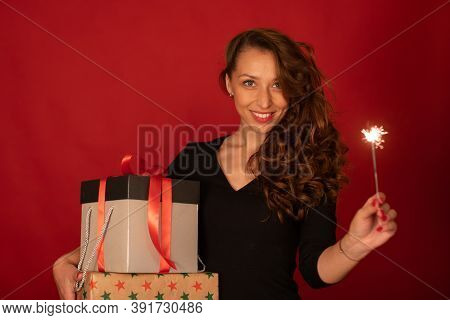 Young Charming Lady With Gift Box And Burning Sparkler Smiling Looks At Camera On Red Background. Ch