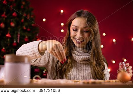 Portrait Of Happy Pretty Long-haired Brunette Girl Decorating Freshly Baked Christmas Cookies On Blu