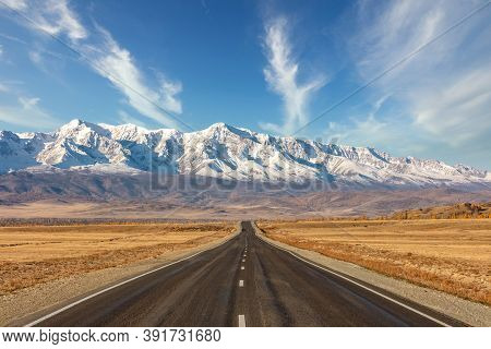 Shot Of A Straight Empty Highway Leading To The Snowy Peaks Of The Kuray Mountain Range. Beautiful B