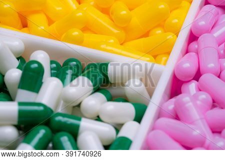 Selective Focus On Capsule Pills In Plastic Box. Pharmaceutical Industry. Pink, Yellow, And Green-wh