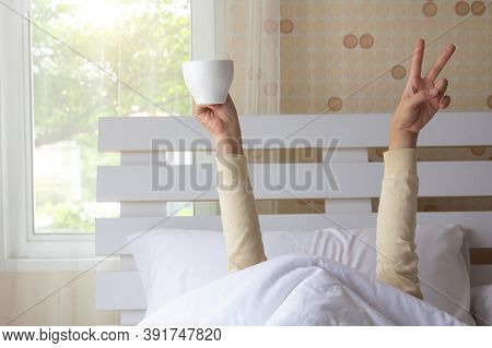 Woman Arm Hands Holding Coffee Cup And Blue Alarm Clock In On Bed In Bed Room. Young Girl With Two H