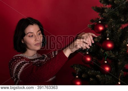 Focused Brunette Girl Dressed In Knitted Winter Pattern Sweater Dresses Up Christmas Tree On Studio 