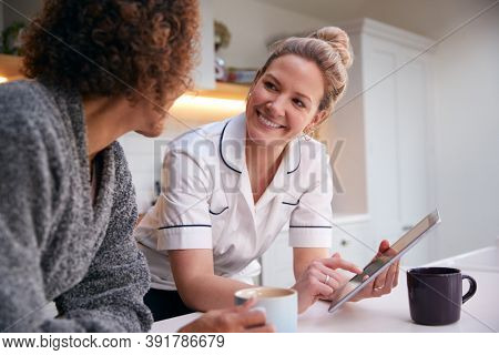 Mature Woman In Dressing Gown At Home Talking With Female Nurse With Digital Tablet