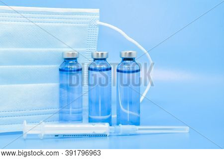 Transparent Medical Ampoules, Syringe And Protective Mask On A Light Blue Background. Concept: Medic