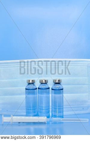 Transparent Medical Ampoules, Syringe And Protective Mask On A Light Blue Background. Concept: Medic