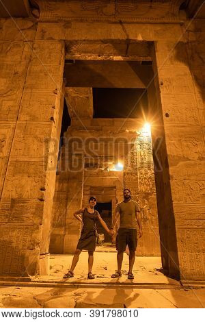 A Couple Of Tourists Between The Columns At Night Of The Temple Of Kom Ombo In Traditional Dress, Th
