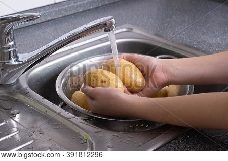 Potatoes Are Washed Under Running Waste Water In The Kitchen For Cooking