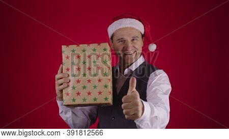 Christmas Surprise. Happy Excited 40s Man In Santa Hat Catching Flying Gift Box And Joyfully Shows T