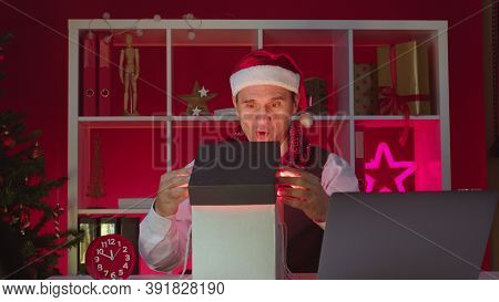Happy 40s Businessman Or Corporate Employee In Santa Hat Opens Magic Gift Box Working Alone In Chris