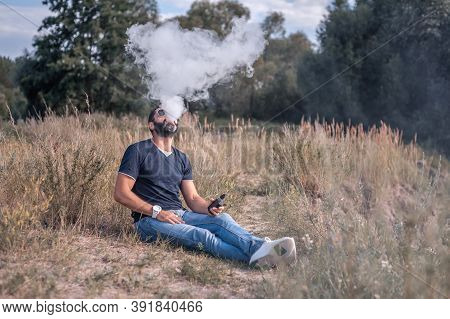 Handsome Vape Man Enjoying An Electronic Smoke Device On The Grass. Non-tobacco Smoking.