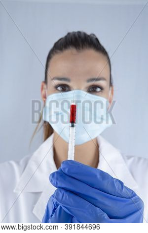 Attractive Female Doctor With Virus Protection Mask And Latex Gloves Carrying A Syringe Of The Sars2