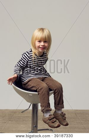 สาวบลอนด์ 3 ปีในกางเกงยีนส์อยู่บนเก้าอี้สูง