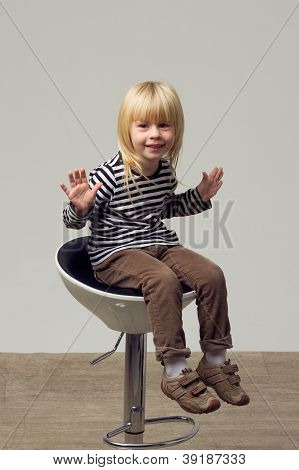 สาวบลอนด์ 3 ปีในกางเกงยีนส์อยู่บนเก้าอี้สูง