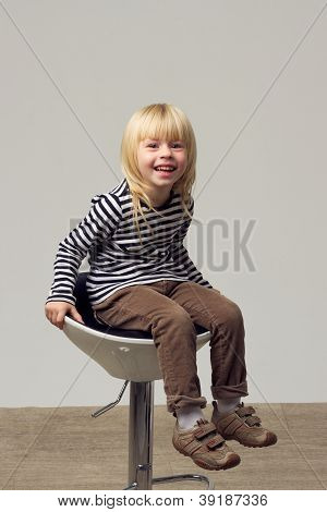 สาวบลอนด์ 3 ปีในกางเกงยีนส์อยู่บนเก้าอี้สูง