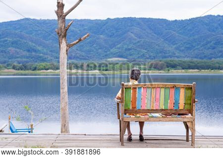 Back View Of A Senior Woman While Sitting On Chairside The Lake. Space For Text