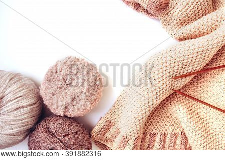 Balls Of Woolen Yarn Of Nude Colors And A Knitted Beige Sweater, Knitting Needles On A White Backgro