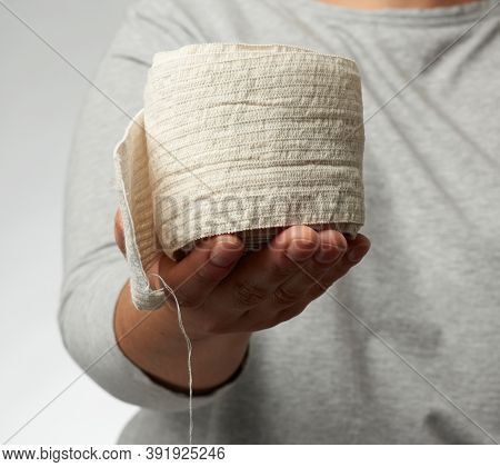 Woman Holds In Hand A White Elastic Bandage For The Body, Gray Background