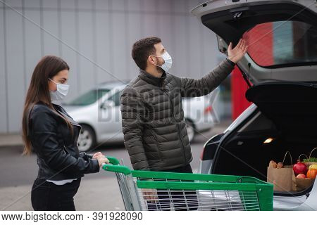 Young Stylish Couple In Protectivemask With Shopping Cart Full Of Fresh Food, Packing Products Into 