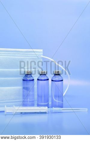 Transparent Medical Ampoules, Syringe And Protective Mask On A Light Blue Background. Concept: Medic