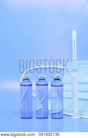 Transparent Medical Ampoules, Syringe And Protective Mask On A Light Blue Background. Concept: Medic
