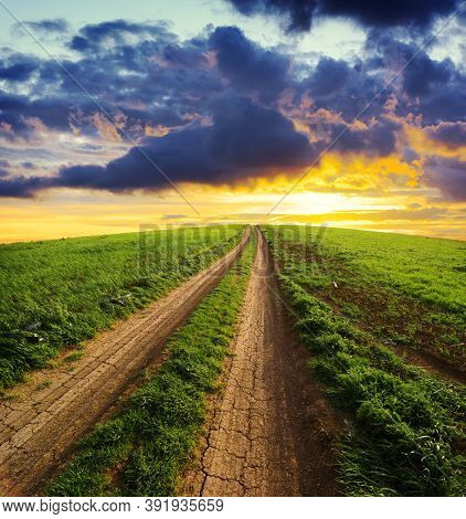 rural path uphill way to a dramatic sky at the sunset crossing a field of grass 