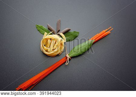 Tagliatelle Pasta, Brown Penne Rigate Pasta,  Red Spaghetti And Laurel Leaves On A Gray Background.