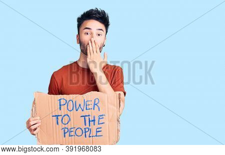 Young hispanic man holding power to the people banner covering mouth with hand, shocked and afraid for mistake. surprised expression 