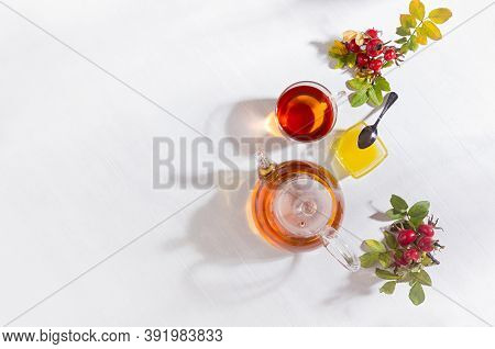 Autumn Healthy Rosehip Tea In Transparent Teapot With Cup, Honey, Dog Rose Branch In Bright Cozy Sun