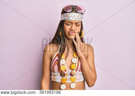 Beautiful hispanic woman wearing bohemian and hippie style touching mouth with hand with painful expression because of toothache or dental illness on teeth. dentist 