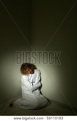 Mentally ill man in strait-jacket in room corner