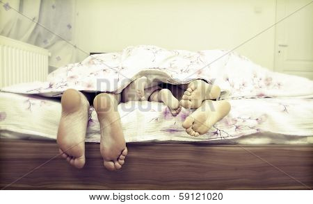 Tree pairs of legs of the happy family in bed - father, mother and baby 