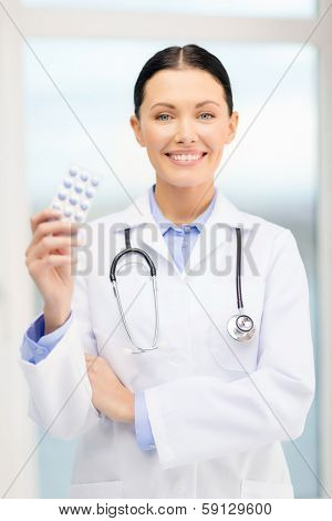 healthcare, pharmacy and medicine concept - smiling young doctor with pills and sthethoscope in cabinet
