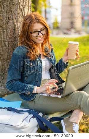 education, technology and internet concept - smiling redhead teenager in eyeglasses with laptop computer and take away coffee or tea
