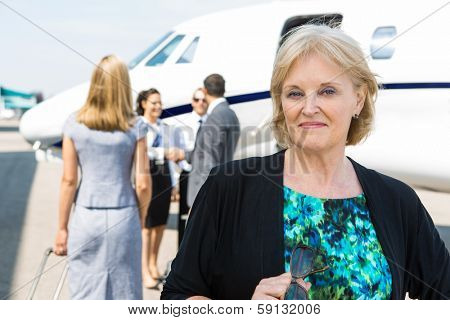 Portrait of confident businesswoman with airhostess greeting business people near private jet