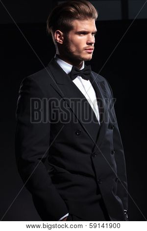 side view of an elegant man with hands in pockets on dark background