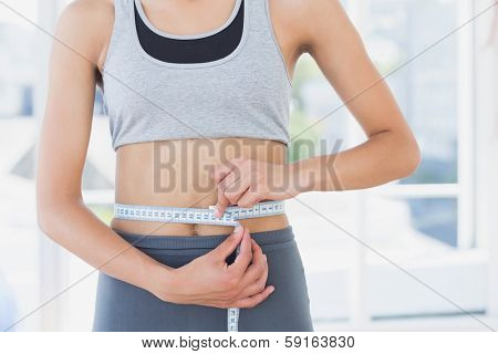 Closeup mid section of a sporty young woman measuring her waist in the fitness studio