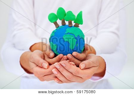 Protecting our environment concept - clay earth with trees held by child and adult hands