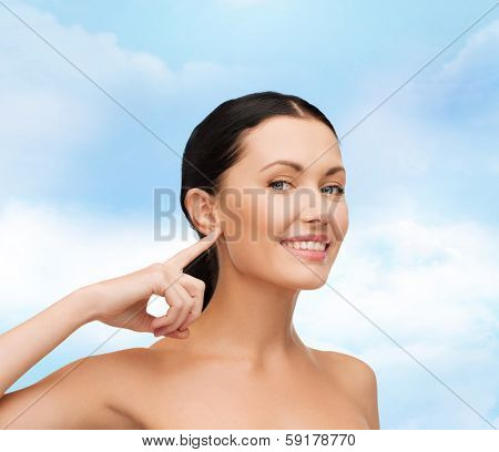 health, spa and beauty concept - clean face of beautiful young woman pointing to her ear