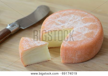 A full wheel brie cheese with a cut slice and a knife