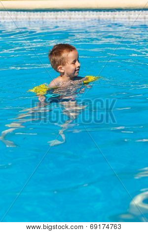 Happy boy swimming with floaties in swimming pool