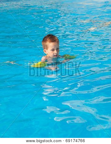Happy boy swimming with floaties in swimming pool