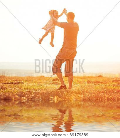 Dad playing with his aughter in a field at sunset