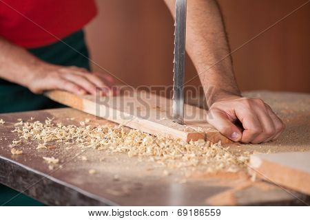 Cropped image of male carpenter cutting wood with bandsaw in workshop