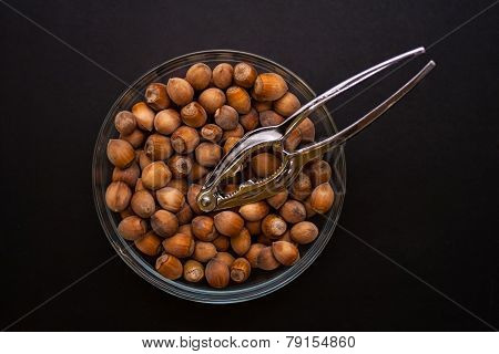 Nuts in glass bowl with nutcracker on black background