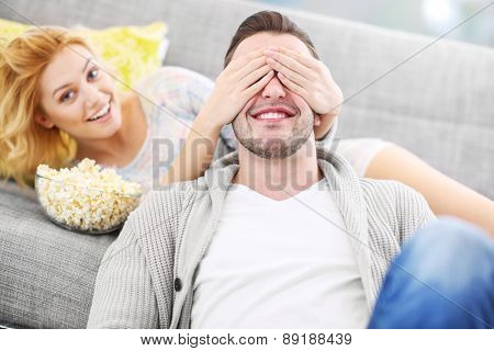 A picture of a woman covering her husband's eyes when watching tv