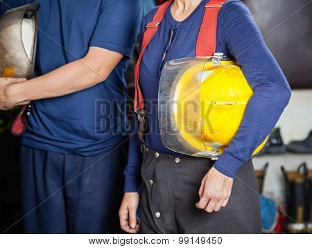 Midsection of male and female firefighters holding helmets at fire station